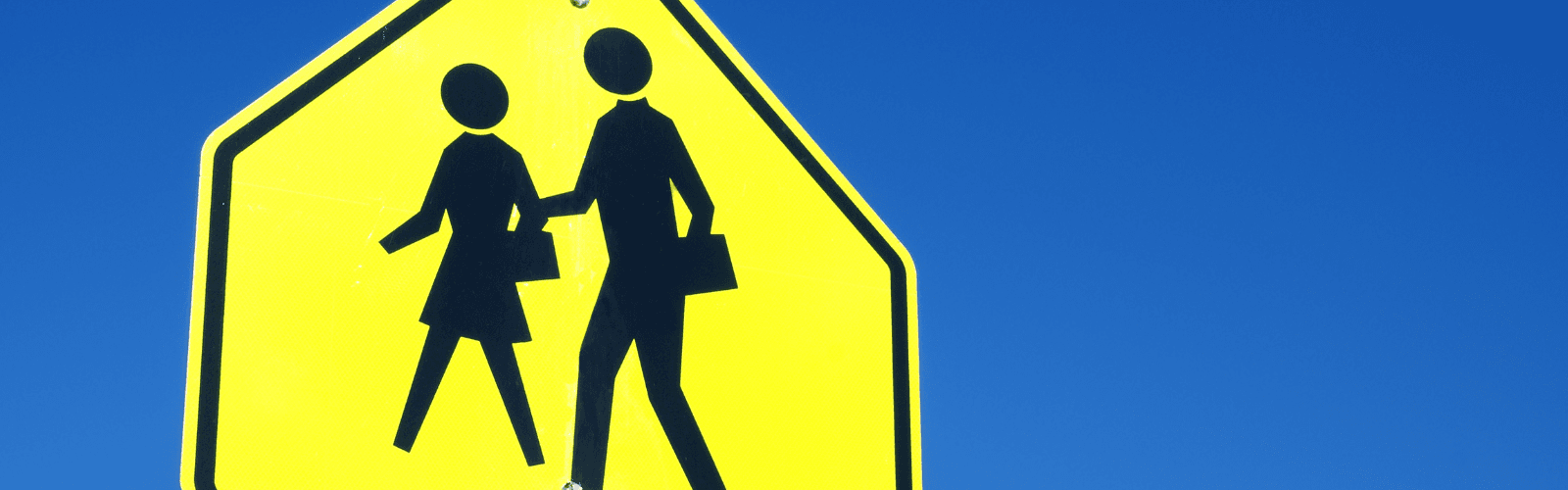 Yellow school crosswalk sign against a blue sky